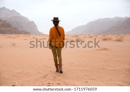 A girl in a cowboy hat and boots is walking on the sand in the Wadi Rum desert in Jordan. Taken from the back in March 2020.
