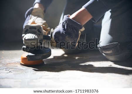 A man in gloves and protective knee pads on the legs grinds the floor with a grinder Royalty-Free Stock Photo #1711983376