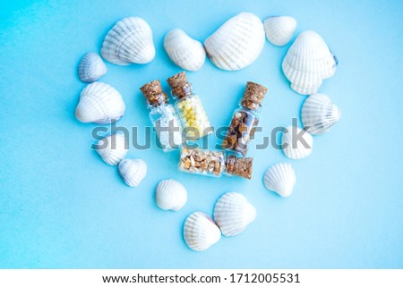 Picture with soft focus of four tiny glass jar with buckwheat, millet, sugar and barley surrounded by shells in forme of heart on blue background, top view. Concept of nutrition, vegetarian products