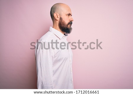 Handsome bald man with beard wearing elegant shirt over isolated pink background looking to side, relax profile pose with natural face with confident smile.