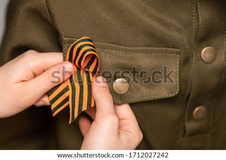St. George's ribbon is fixed by the hands of a girl on the military uniform. Concept of memory, symbol of Victory Day.  