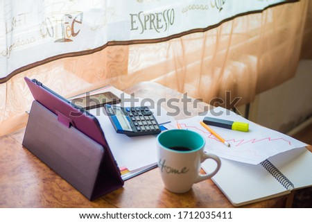 

On the home table are stock and finance charts with a calculator, a coffee mug, a pencil, a marker pen, two notebooks, a smartphone and a tablet for remote work. Work at home.