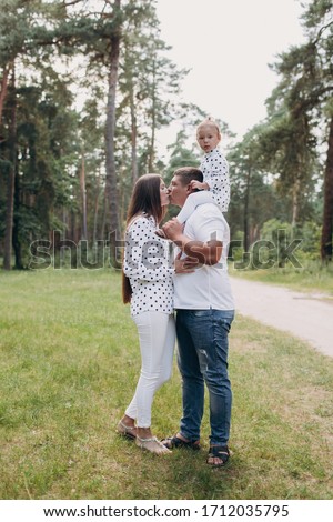 Daddy's carrying a baby daughter on his shoulders in the park, forest. The concept of summer holiday. Father's, mother's, baby's day. Spending time together. Family look. Couple kissing.