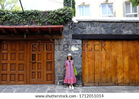 An Asian female tourist standing, posing for a picture in front of a rich house in Coyoacán (Place of Coyotes), Mexico City, Mexico.
