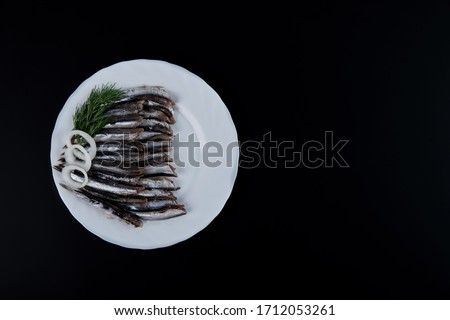 European sprat, hamsa lies on a white plate isolated on a black background with cherry tomato and green onions