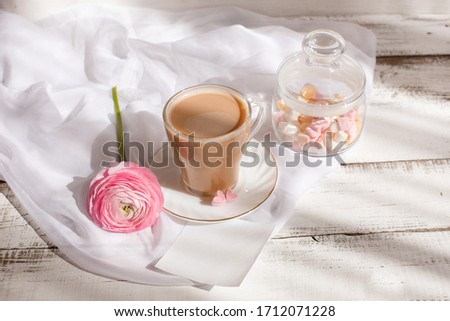 good morning card in pink. A Cup of coffee, a marshmallow and a pink flower , an empty piece of paper, a note , space for text on a light wooden background.
