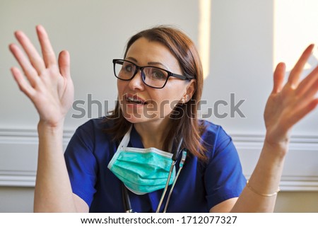 Portrait of talking doctor woman in blue uniform with stethoscope mask sitting in office, video conference call. Online medical advice and assistance