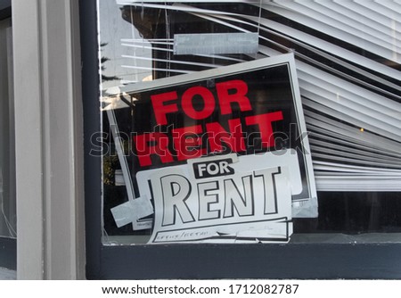 A crooked "For Rent" sign displayed in a window with crooked, broken blinds