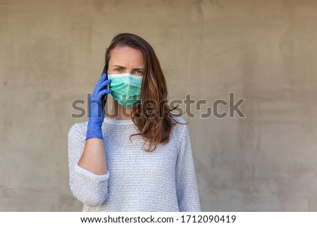 Young woman wearing medical face protection mask and gloves as part of covid-19 pandemic prevention and protection campaign, having a phone conversation