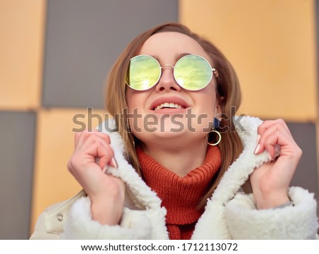a positive girl in a brown jacket and white sheepskin coat and sunglasses smiles. close up. reflection of the sky in glasses.