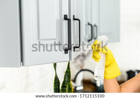 Close-up picture of hands in yellow protective rubber gloves is cleaning handles of kitchen cabinets at home. House cleaning and disinfection.