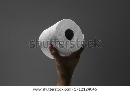 One hand holding a roll of toilet paper with spotlight effect and isolated dark grey background