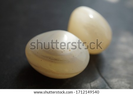 White agate tumbled tpebble on gray slate background, lit by the sun  Royalty-Free Stock Photo #1712149540