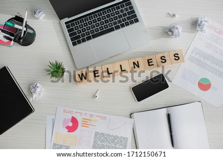 top view of workplace with business documents, laptop, smartphone and alphabet cubes with wellness word