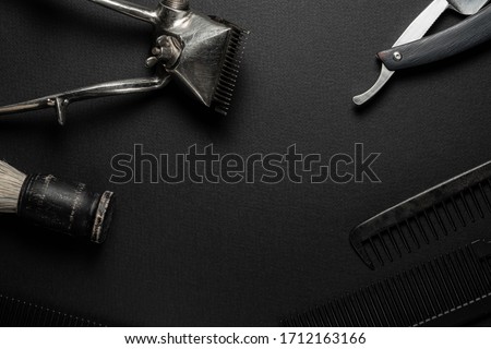 On a black surface are old hairdresser tools. vintage hand-held hair clipper, hairdressing scissors, combs, razor, shaving brush. black monochrome. horizontal orientation. flat ley
