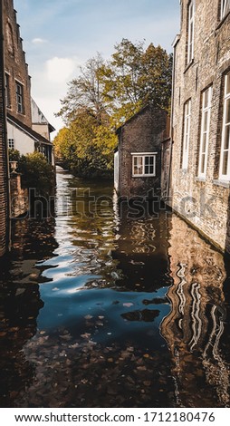 Outdoor scenic landscape from Bruges, Belgium. Beautiful reflection in the water of river in the city center of Brugge. Brick buildings and dark moody colors, view from the bridge. Popular destination