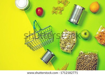 Online shopping food cans, pasta, spaghetti, apples, cereals, lemons, tomatoes and a food basket on a green-yellow background, top view, flat lay. Home Food Delivery Concept