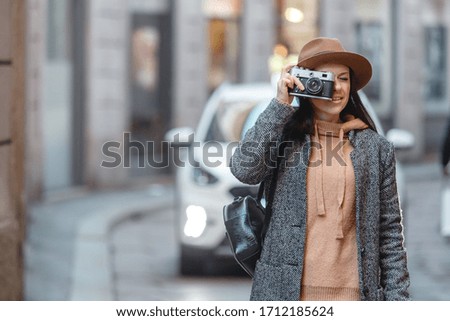 A beautiful girl is a tourist in a gray coat and and a fashionable brown shlape, walks and takes pictures
