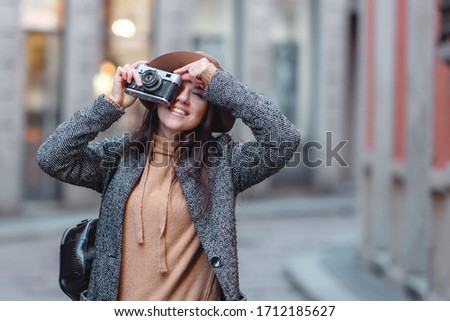 Beautiful girl tourist in a gray coat and with a backpack on his shoulder walks and takes pictures of the building