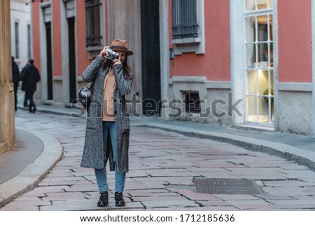 Hiker girl with a camera in her hands smiles against the background of a small old street in orange tones