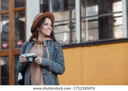 A young girl looks around, smiling against the background of an orange tram passing by