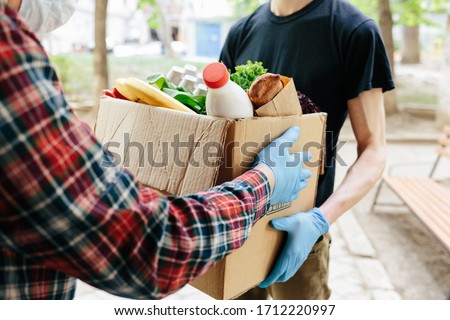 Delivering food to senior citizens in quarantine during Covid-19 Coronavirus epidemic. Courier in black shirt medical gloves Royalty-Free Stock Photo #1712220997