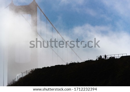 Close up of Golden Gate bridge in low clouds and silhouette of people standing on vista point.