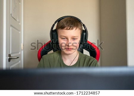 Active teen boy wearing headphones does homework using laptop, tired being at home. Concept of online learning. Chat with your teachers online. Distance education, self-isolation. Close up of gamer