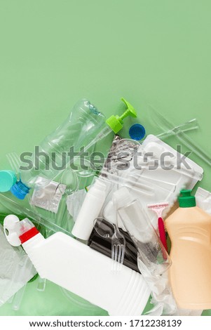 Plastic dishes and bottles on a green background. Ecology and waste management concept. Vertical photo.