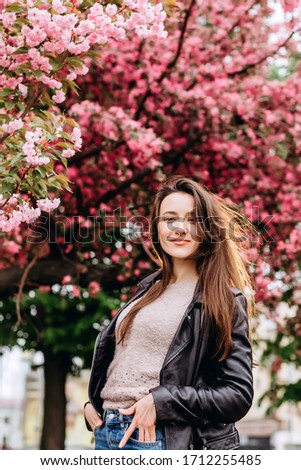 Outdoor portrait of young beautiful fashionable lady posing near flowering tree. Female beauty and fashion. City lifestyle. girl on background of pink flowering trees. Closeup portrait girl in spring