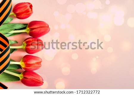 Red tulips with St. George ribbon on colorful background with sparks. Victory day gift card or Fatherland defender day.