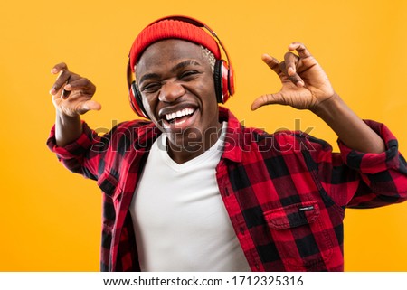 funny attractive african black man stylishly dressed with a grimace on his face listens to music with headphones on a yellow studio background