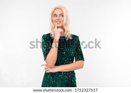 girl in elegant green shiny dress makes a pensive look on a white studio background