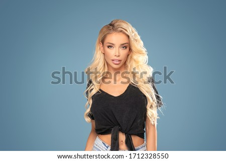 Pretty young fashionable blonde woman posing on blue pastel studio background dressed in hipster style outfit.