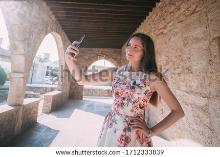 Young woman takes a selfie on the background of an ancient temple on a sunny day. A girl is photographed near the ancient stone walls of the church.