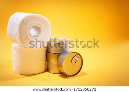 Toilet paper rolls next to canned goods, on top of yellow background, with available copy space. 