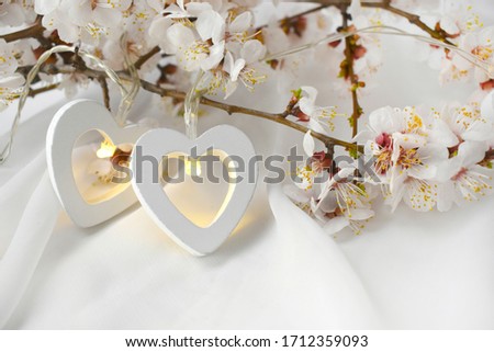 Romantic wedding composition with blooming  branch, two hearts  on white silk background. Elegant greeting concept for Valentines day, Mothers day, Womans day. 