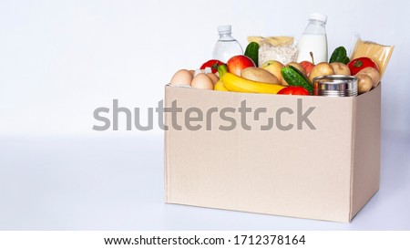 Various grocery items in cardboard box on gray table. Food box with fresh vegetables, fruits, cereals, pasta, milk, eggs and canned goods. Food delivery or donation concept. Copy space. Royalty-Free Stock Photo #1712378164