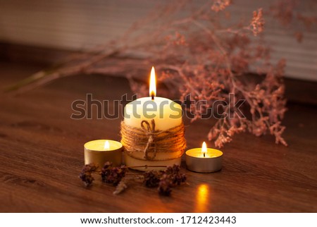 Aromatherapy flame closeup picture. Beautyful burning light yellow creme vanilla candles with wooden background. Evening spa lightens and dry flowers