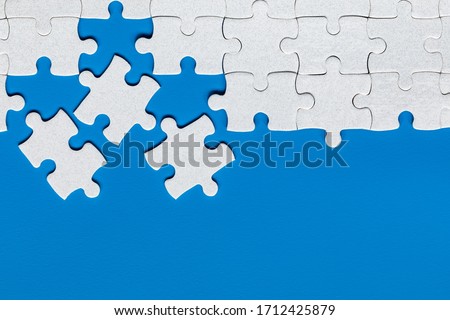 Unfinished white jigsaw puzzle pieces. Fill in pieces of the jigsaw puzzle. Complete the jigsaw puzzle with the missing pieces. Fragment of a folded white jigsaw puzzle. Royalty-Free Stock Photo #1712425879
