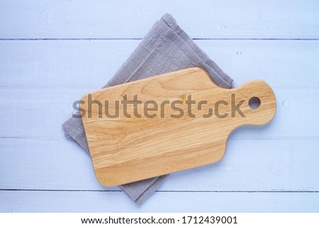 Top view above of Wooden chopping board with napkin on white table background. Wood Cutting board with handle and hole for hanging. Empty utensil with copy space.