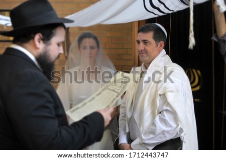 Rabbi reading the Jewish Marriage Contract (Ketubah) to Jewish bride and a bridegroom in modern Orthodox Jewish wedding ceremony in synagogue.Real people. Copy space Royalty-Free Stock Photo #1712443747