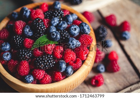 blueberries and raspberries, blackberry in a wooden bowl on old wood background Royalty-Free Stock Photo #1712463799
