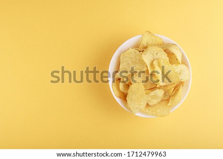 Crispy potato chips in bowl on yellow background, top view
