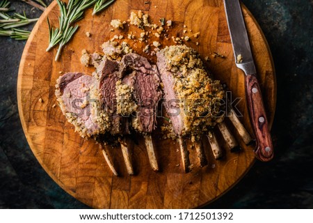 Close up of crusted lamb ribs cutlets with bone rar medium roasted on wooden cutting board with knife and herbs. Top view. Meat food Royalty-Free Stock Photo #1712501392