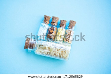 Picture with soft focus of five tiny glass jar with rice, buckwheat, millet, sugar and barley on blue background, top view. Concept of nutrition, vegetarian products. Empty copy space for text.