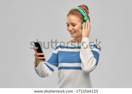 music, technology and people concept - smiling teenage girl in headphones with smartphone over grey background
