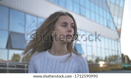 Girl in a white sweater with a sad look stands on the background of a business building