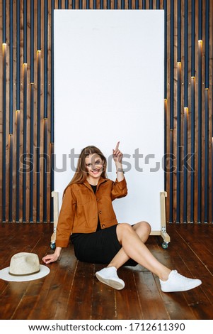 A model girl in a brown jacket with a light hat points to a white canvas on which you can write a slogan or advertising information