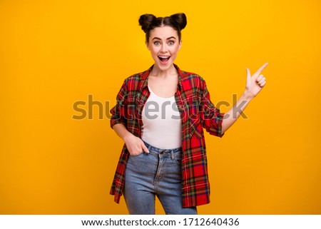 Photo of pretty funny lady teenager open mouth good mood directing finger empty space advising novelty product wear casual plaid shirt jeans isolated vivid yellow color background